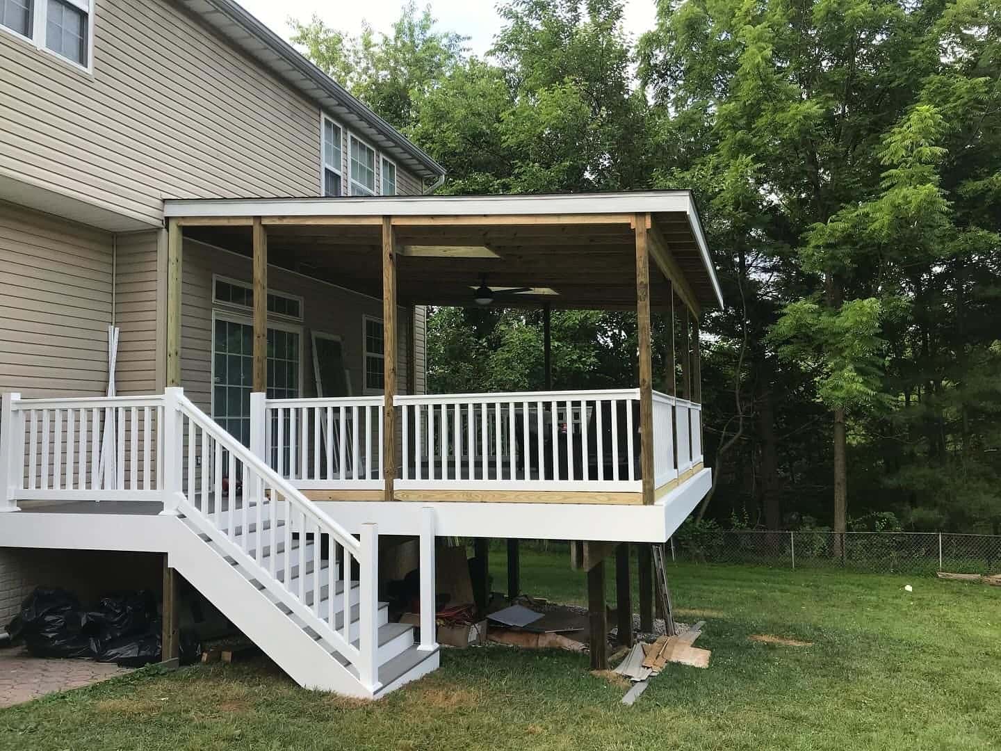 Covered deck built by Roso with a shed roof, ceiling fan, white railing, and stairs to the lawn behind a two-story home